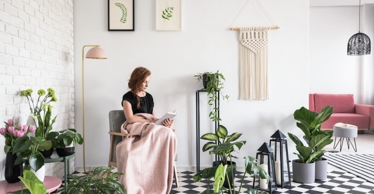 Young girl reading a book, covered with blanket in a living room interior with plants and checkered floor